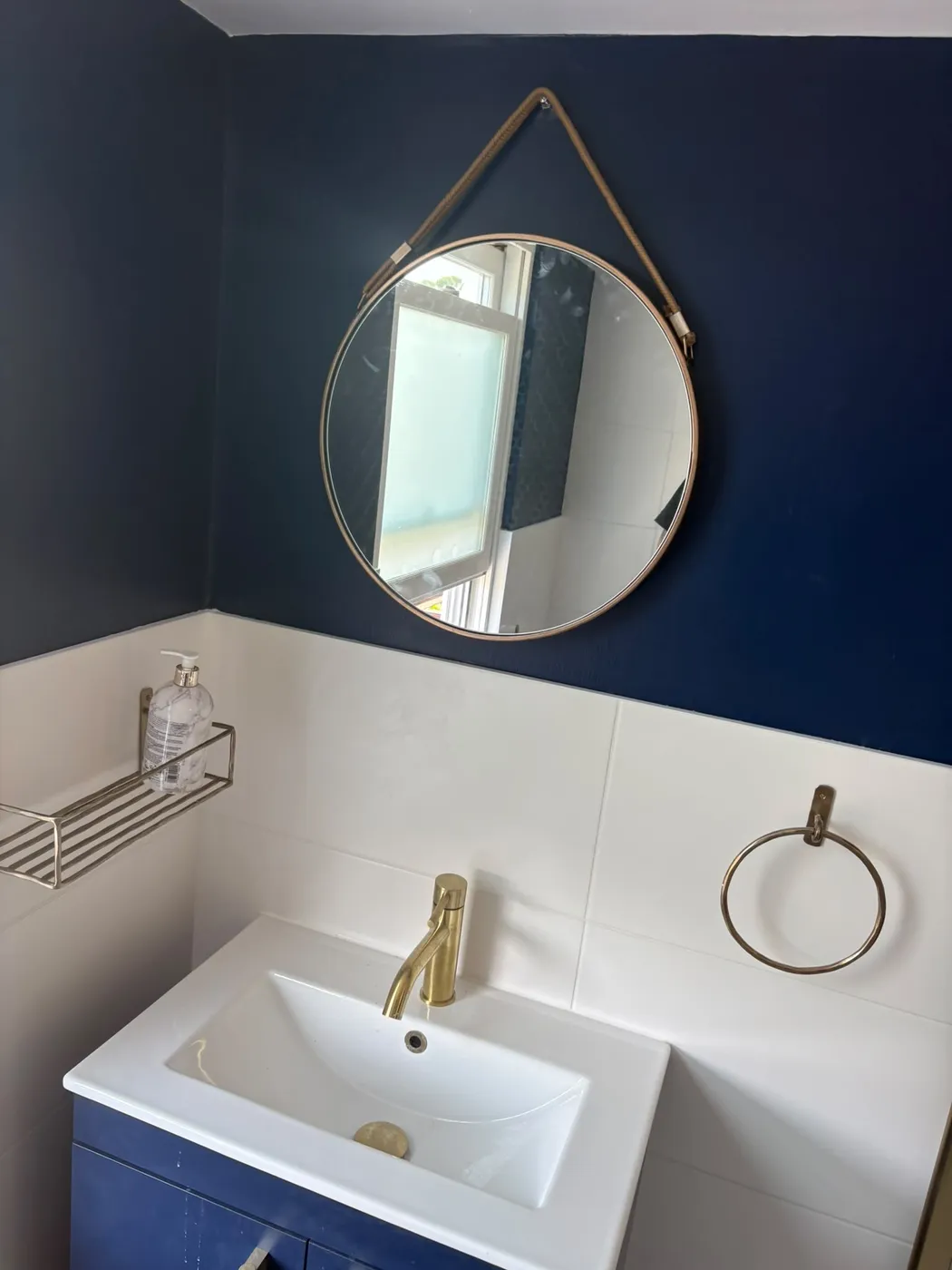 Navy blue bathroom wall with brushed brass tap, round hanging mirror and white basin vanity in a refurbished London bathroom.
