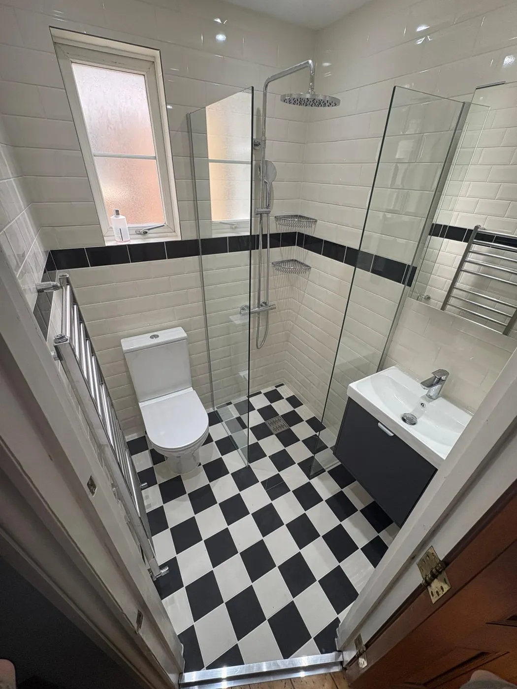 Traditional-style shower room with black-and-white chequerboard floor, white metro tiles with black border and corner glass shower.