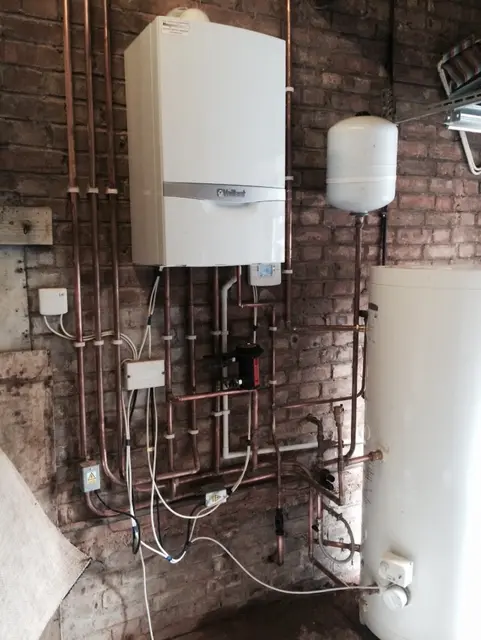 Vaillant boiler and hot water cylinder installation with copper pipework and wiring centre mounted on exposed brick.