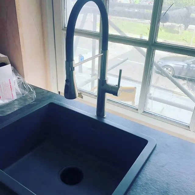 Navy composite kitchen sink with matching pull-down spray mixer tap installed beneath a Crittall-style window.