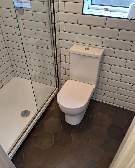 Newly installed shower room with corner glass enclosure, white metro wall tiles, close-coupled WC and grey hexagon floor tiles.