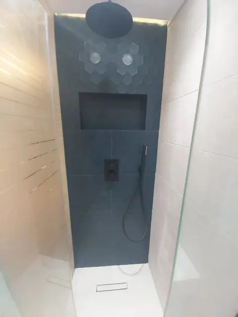 Walk-in shower with dark slate feature wall, hexagon accent tiles, recessed niche and matt black rainfall shower head.